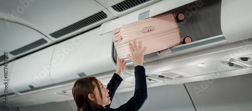 фотографія Happy  traveler stowing personal pink suitcase securely inside airplane cabin ov