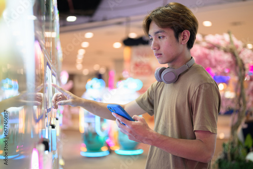 Young Thai man using vending machine in shopping mall with headphones
