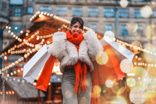 Obraz na plátně Excited young woman in winter outfit enjoys shopping with colorful bags in festi