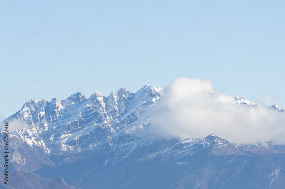 Fototapeta premium Veduta panoramica di cime innevate con soffici nuvole e un cielo azzuro pristino, Italia, Regione, Lombardia, Provincia di Lecco