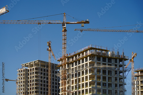 Fotografie Yellow tower cranes working on the new hi-rise residential buildings in the city near the river