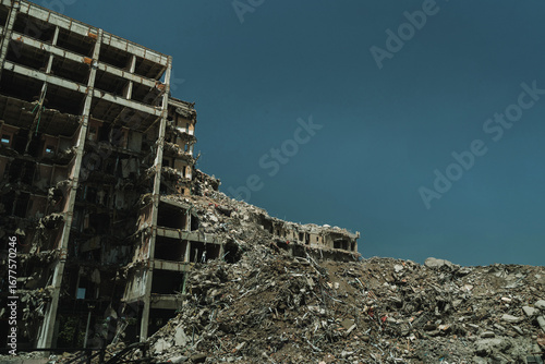 Bild auf Leinwand A massive concrete apartment building lies in ruins, partially collapsed with a field of debris, aftermath of demolition, earthquake, or urban disaster