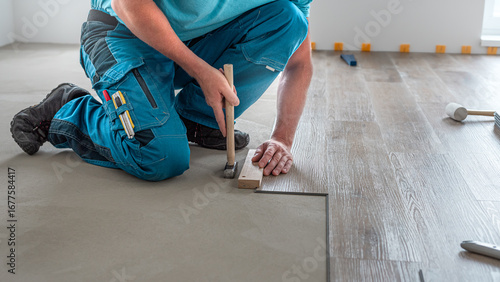 Floating floor work. The worker taps the board of vinyl plank to lock the click system. He is using hammer and wooden plank.