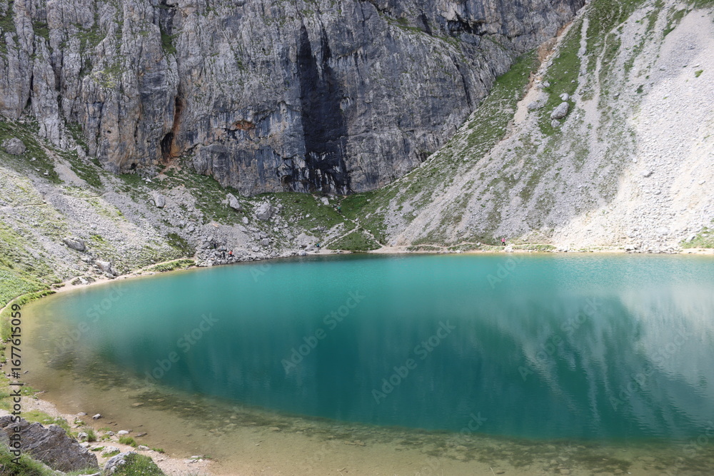 Naklejka premium Trentino, Italy - July 29, 2025: Panoramic view of the majestic Piz Boe and the surrounding Dolomite peaks, with lush green valleys and scattered snow, under a clear blue sky. beautiful view to Lake b