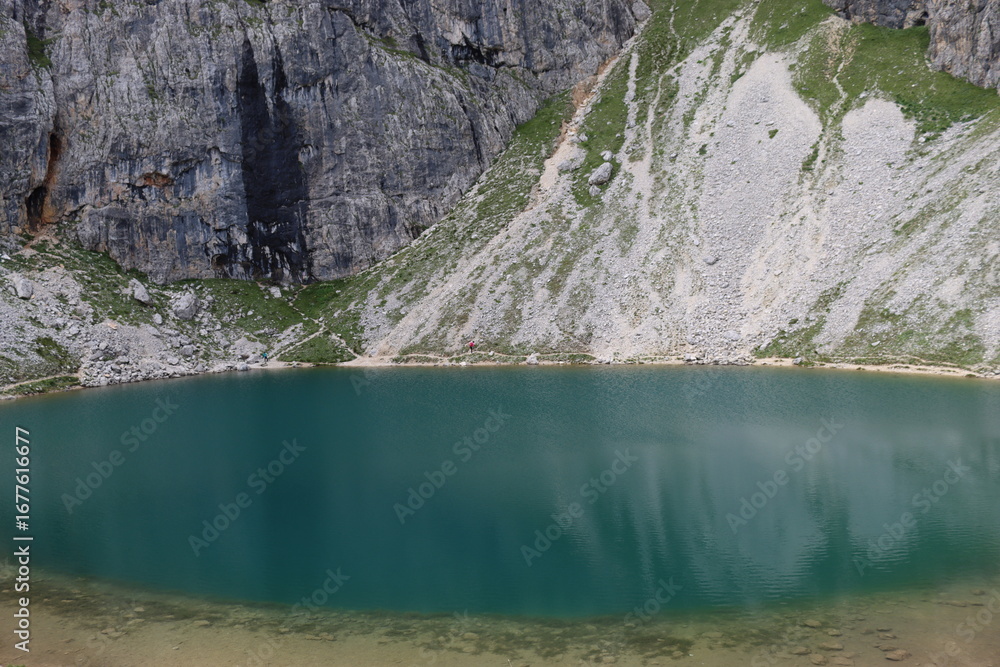 Naklejka premium Trentino, Italy - July 29, 2025: Panoramic view of the majestic Piz Boe and the surrounding Dolomite peaks, with lush green valleys and scattered snow, under a clear blue sky. beautiful view to Lake b