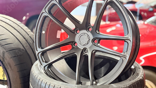 Car alloy wheel on tire, front view close-up in workshop, multi-spoke rim with central hub, product photo with shallow depth of field and blurred background