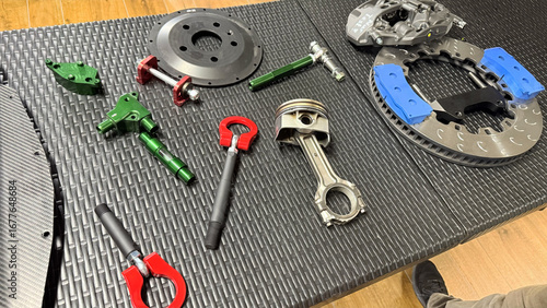 Wallpaper Mural Automotive parts on workshop table, Top View: brake disc, ventilated rotor with blue segments, caliper, piston and connecting rod, red tow hooks, green brackets, ratchet wrench on textured surface Torontodigital.ca