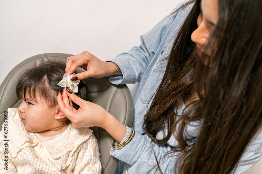 Fototapeta premium Mother putting a white flower hair clip on her baby girl's hair