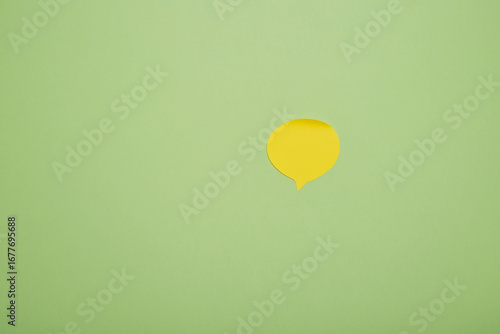 Yellow speech bubble paper cutout on green background, minimal concept for message or communication