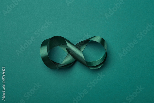 Satin green ribbon arranged in infinity symbol on teal background, representing awareness, hope and continuity