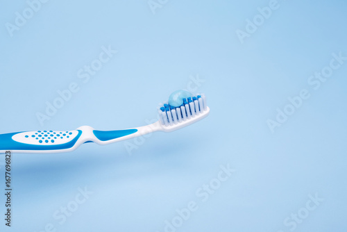 White and blue toothbrush with fresh blue gel toothpaste on bristles against pastel background
