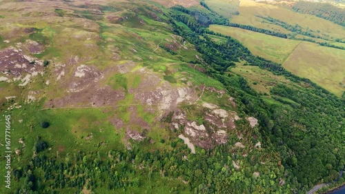 aerial drone shot flyover of England Lake District hill mountain covered in grass and trees with lake water just in view in summer