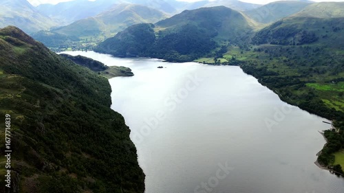 Aerial drone flyover of ullswater lake in England Lake District inside a valley surrounded by mountains and hills in nature in summer with clouded skies