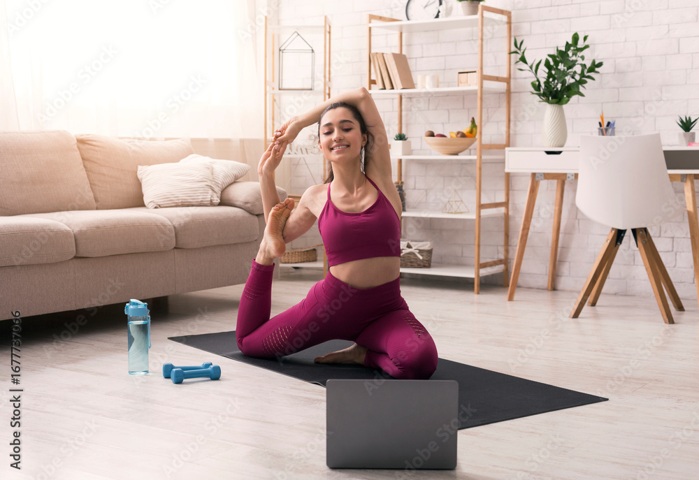 Fototapeta premium Sports during self isolation. Beautiful girl watching online training class and doing yoga at home