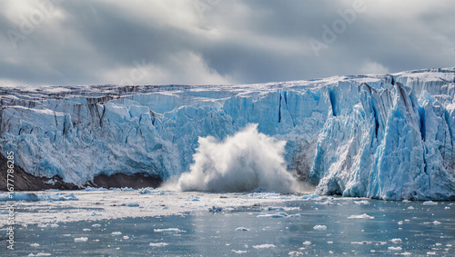 A massive glacier in the arctic is shown calving, with a large chunk of ice breaking away and crashing into the sea. The dramatic splash and deep blue ice walls highlight the impact of climate change.