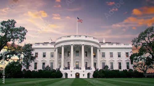 The iconic White House in Washington D.C. at sunset, featuring its grand facade, lush green lawn, and an American flag flying proudly.