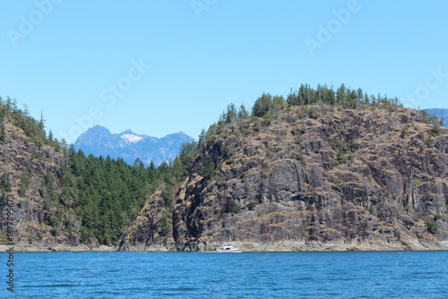 Summer boating in Desolation Sound near Tenedos Bay, with rugged cliffs, forested shores, and calm blue water under a clear, bright sky