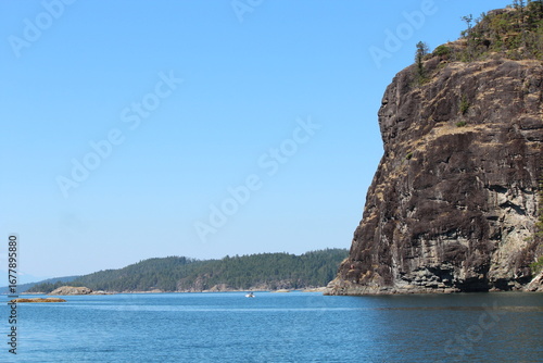 Summer boating in Desolation Sound near Tenedos Bay, with rugged cliffs, forested shores, and calm blue water under a clear, bright sky