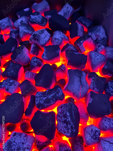 Burning charcoal briquettes glowing with flames, showing high heat for grilling and cooking outdoors with fiery coals.