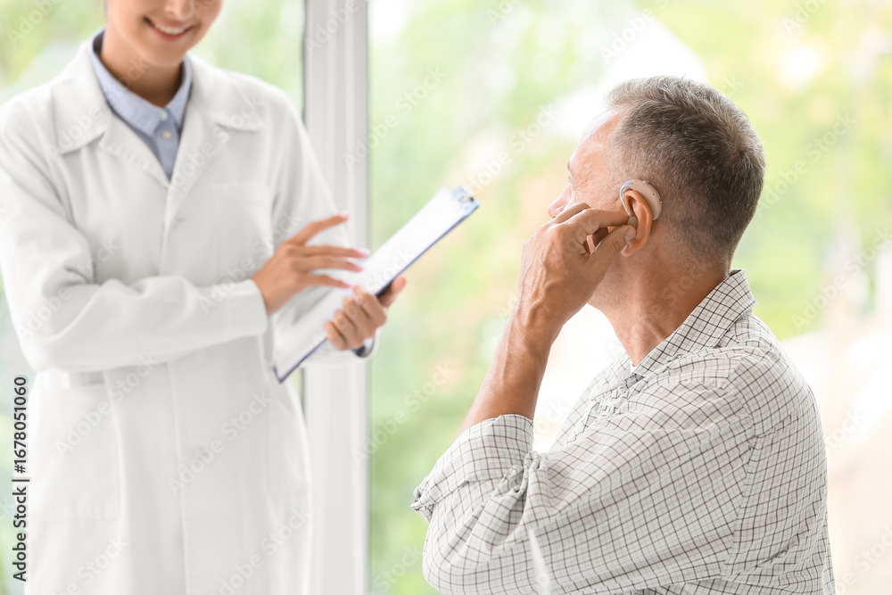 Fototapeta premium Mature man with hearing aid visiting doctor in clinic