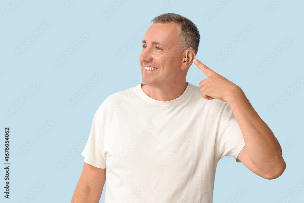 Obraz premium Mature man pointing at hearing aid on blue background