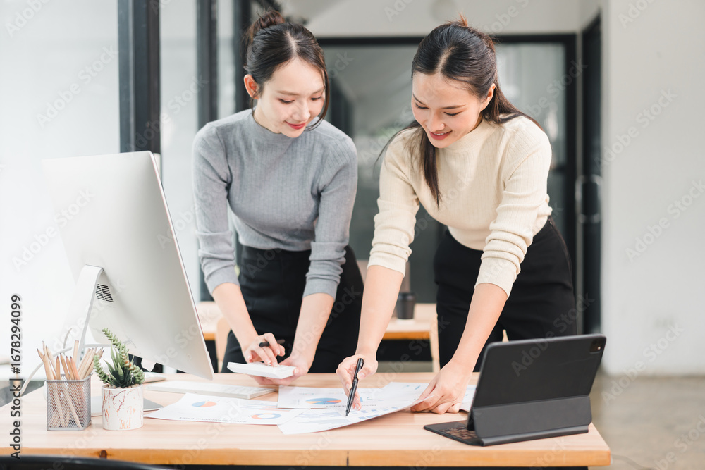 Fototapeta premium Young woman working on office documents with colleague, reviewing chart and pointing at paper, collaborative planning and focused discussion