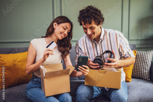 Canvas Print A happy young couple opens a cardboard package at home, smiling as they discover their purchase