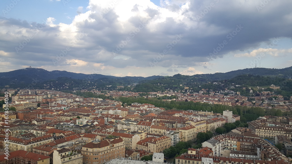 Naklejka premium A panoramic view of the Torino skyline, with rays of sunlight breaking through the clouds and the majestic Alps visible in the background.