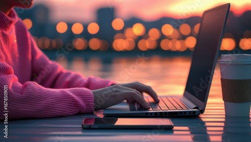 A person types on a laptop computer outdoors at sunset, with a warm, soft light illuminating the scene.