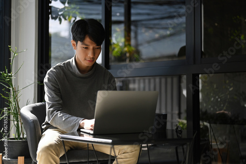 Focused freelance working in a relaxed indoor-outdoor area, dressed in smart casual, and using a minimalist setup