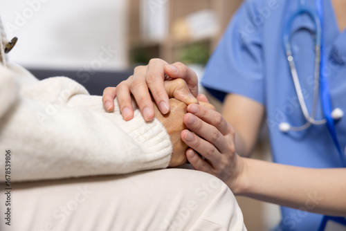 Asian Compassionate healthcare worker holding elderly patient hand, showing care and support in medical setting with stethoscope visible on uniform