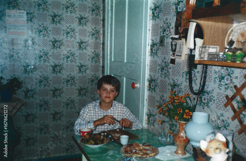 Boy eats at kitchen table, captured in analog photography style from 1990s in Ukraine.