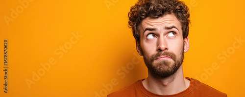 Man with curly hair looks up thoughtfully against a vibrant orange background
