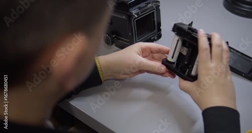 An over-the-shoulder view of a photographer loading 120 film. Their hands carefully place a new roll film spool into the insert of a medium format camera back before shooting.
