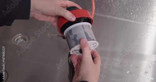 The moment of truth in analog photography. A photographer's hands carefully pull the wet, developed 120 film negative from its developing reel over a darkroom sink.