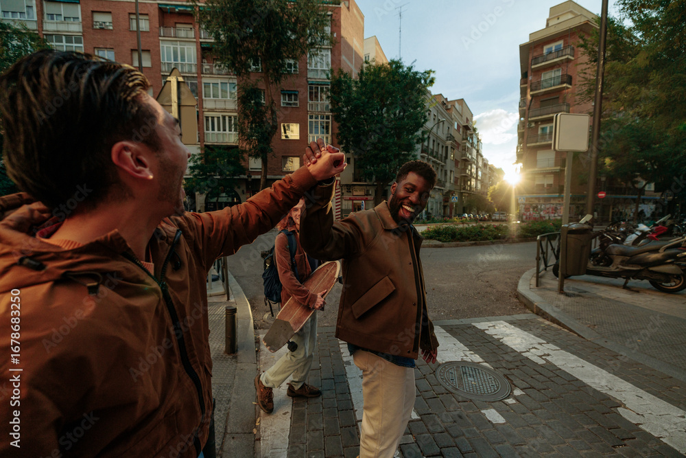 Obraz premium Happy friends joining hands crossing the street at sunset in Madrid