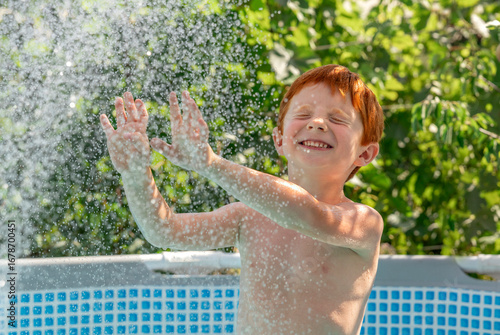 Red-haired child playing cheerfully in outdoor pool on a sunny summer day