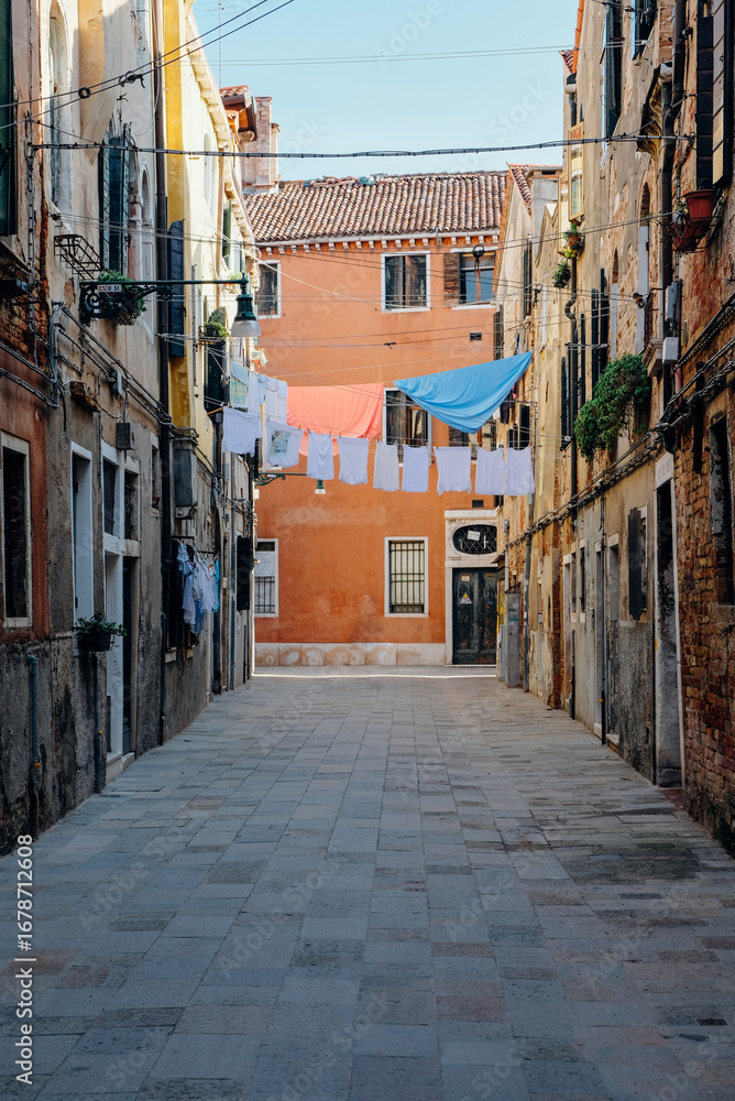 Fototapeta premium Typical Venetian view with narrow street, colorful ancient buildings and laundry hanging to dry.