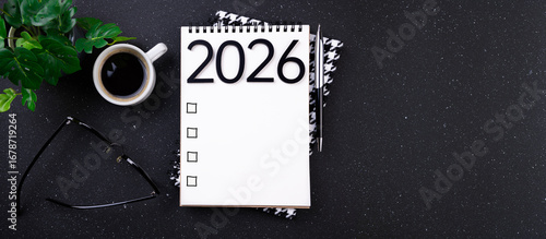 New year resolutions 2026 on desk. 2026 goals list with notebook, coffee cup, plant on black table. Resolutions, plan, goals, action, checklist, idea concept. New Year 2026 resolutions, copy space