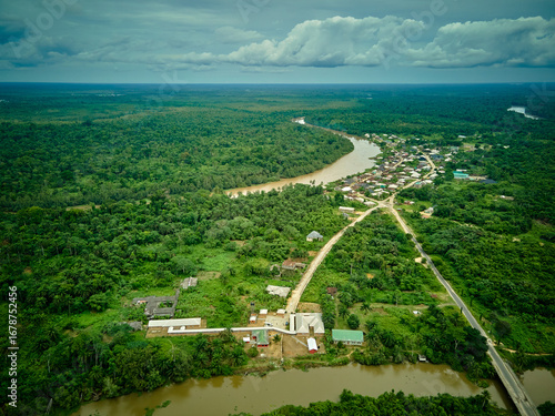 Aerial view of the muddy river snaking through dense green forest, alongside a small settlement under a cloudy sky, Ogbia, Bayelsa, Nigeria.