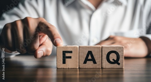 A hand pointing to wooden blocks spelling faq on a wooden surface in a close up shot