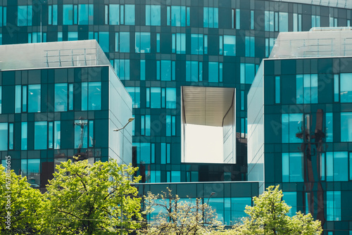 Modern glass commercial exterior of office building architecture. Window covered abstract building with green trees in front. Contemporary high rise structures. Business and success concept