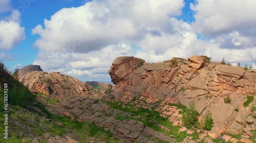 Rock formation resembling a human face among mountain ridges and greenery.