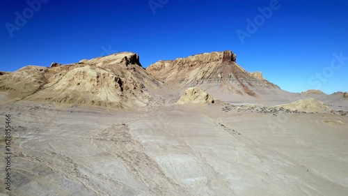 Rocky cliffs and canyon formations of the Mangystau desert under a bright blue sky.