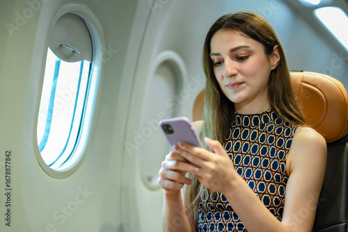 White female passenger sitting by airplane window holding mobile phone turned off, concept of flight preparation, safe travel, aviation regulations, airline comfort, and modern passenger lifestyle.