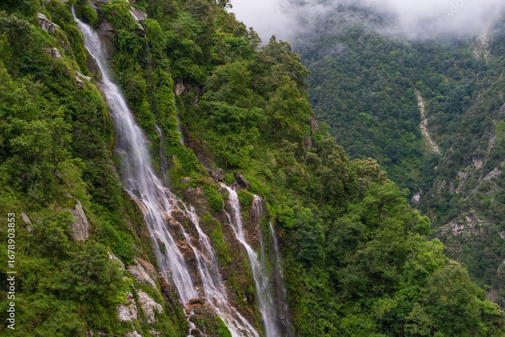 Fototapeta premium Cascading waterfall in lush green mountains.