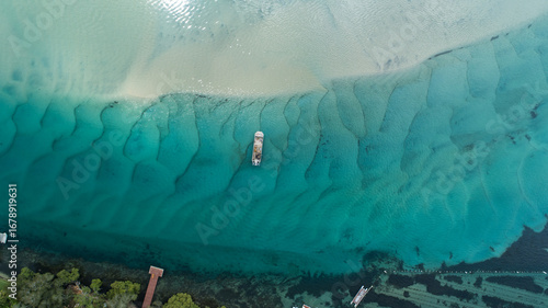 Aerial view of a boat resting on the shallow turquoise waters near a wooden pier against the backdrop of lush greenery, Queensland, Australia.