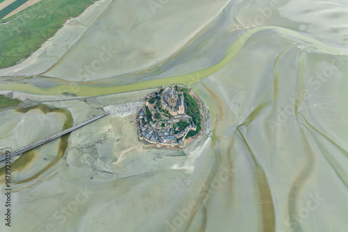 Aerial view of the Mont Saint-Michel, a rocky tidal island crowned by its iconic abbey, rising majestically from the vast, shimmering mudflats, Normandy, France.