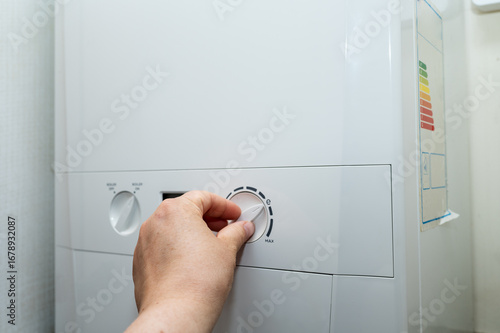 A hand turning the control knob on a household boiler to regulate heating and hot water. Concept of energy usage, bills, and heating systems in England. High quality photo