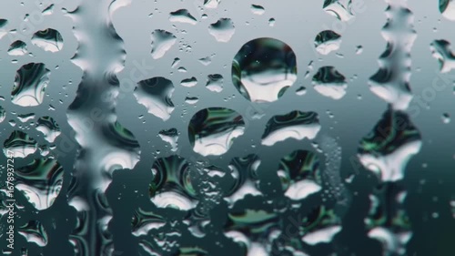 Close-up of water droplets on glass, reflecting blurred green nature. Wet window pane texture.